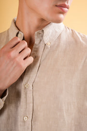 Close-up of a person wearing a beige button-up shirt against a yellow background