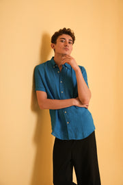 Person wearing a blue shirt and black pants against a beige background